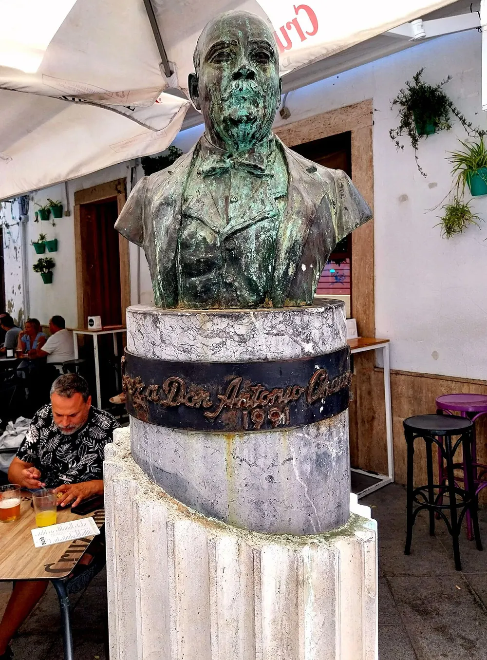 赫雷斯一座石基上的歌手安東尼奧·查孔（Antonio Chacón）綠色銅像半身像，後方有咖啡桌