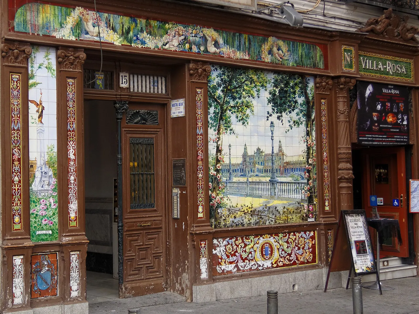 前Villa Rosa門面上的一幅磁磚板，描繪一座宏偉廣場與路燈，旁邊是一扇編號15的深色木門