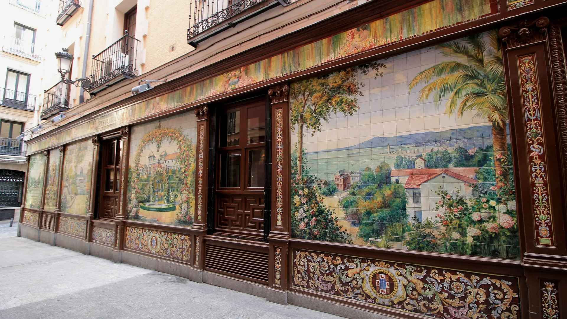 馬德里Plaza de Santa Ana上昔日Villa Rosa的磁磚外牆：一幅大型彩繪陶瓷壁板，描繪有棕櫚樹與紅瓦房舍的海灣景致，上方以深色雕花木框環繞，下方則是綴有裝飾的磁磚基座